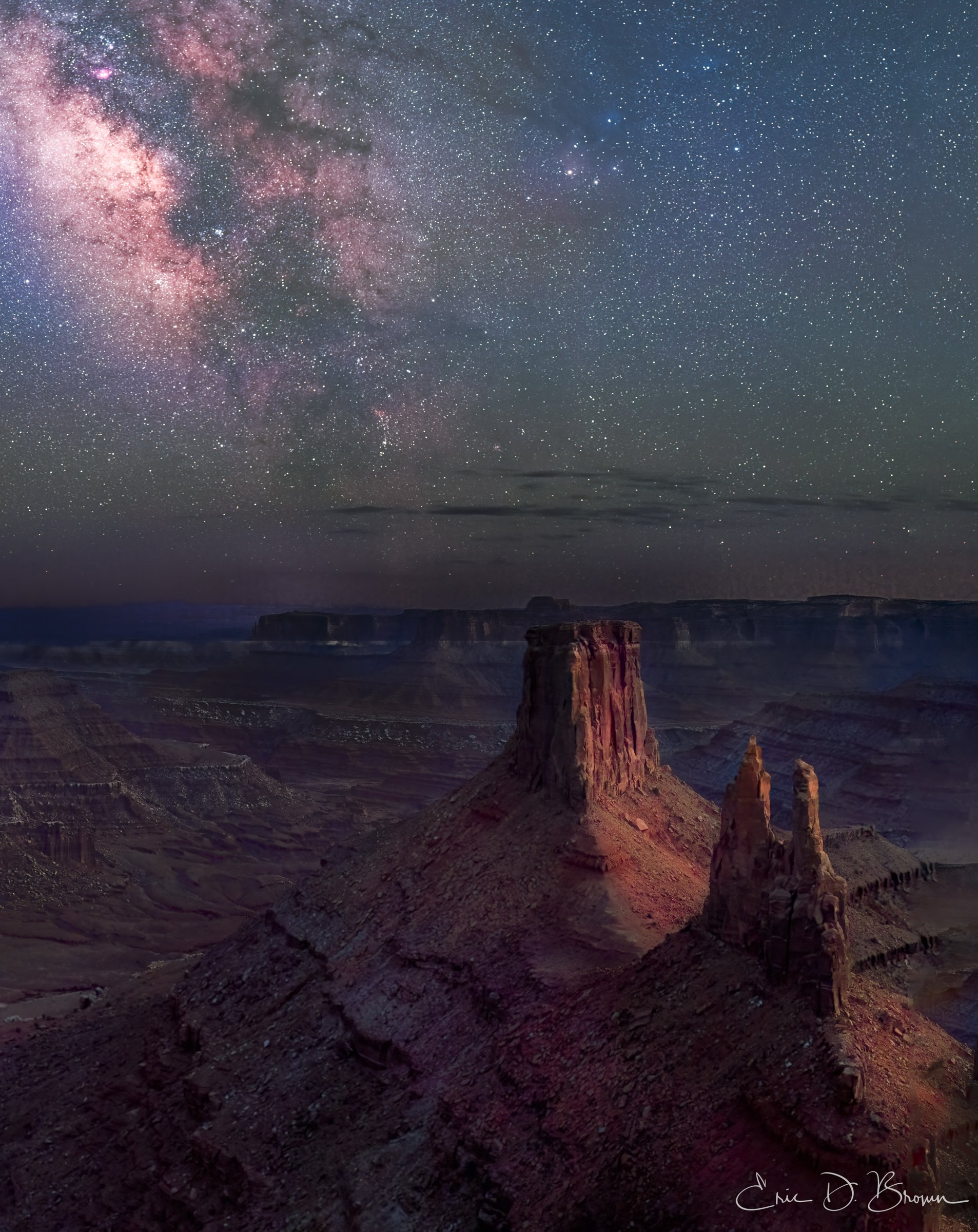 The Magic of Marlboro Point After Dark -  In the stillness of night, ancient rock formations stand guard beneath a cosmic ocean. The Milky Way stretches across the sky, painting our galaxy in vibrant pinks and blues over the iconic mesas of Marlboro Point. Located near Dead Horse Point State Park and Canyonlands National Park in Utah, this remarkable landscape transforms under starlight, revealing the perfect harmony between earth and sky.

