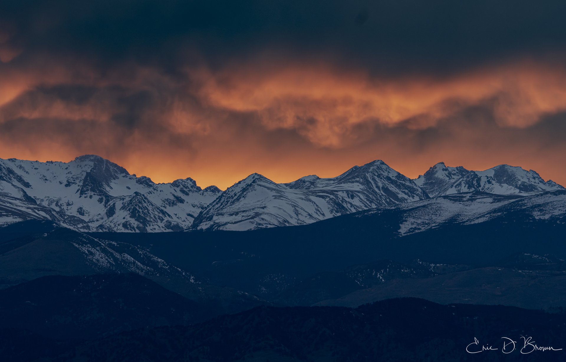 Colorado Rocky Mountain Alpenglow: Winter Peaks at Sunset - Experience the breathtaking majesty of Colorado's Rocky Mountains as twilight paints these snow-capped peaks in rich amber and violet hues. This dramatic mountain landscape showcases the rugged beauty of the Continental Divide, where towering summits meet fiery skies—a quintessential Colorado high country moment captured during the golden hour.