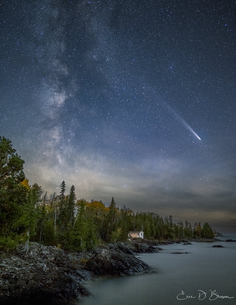 Michigan's Night Sky Spectacle: Comet Tsuchinshan-ATLAS and the Milky Way - This breathtaking night sky capture showcases Comet Tsuchinshan-ATLAS streaking across the star-filled Michigan sky, with the Milky Way rising majestically above a solitary cabin nestled among the trees along Lake Superior's rocky shoreline. The juxtaposition of celestial majesty and earthly wilderness creates a timeless moment of natural wonder.